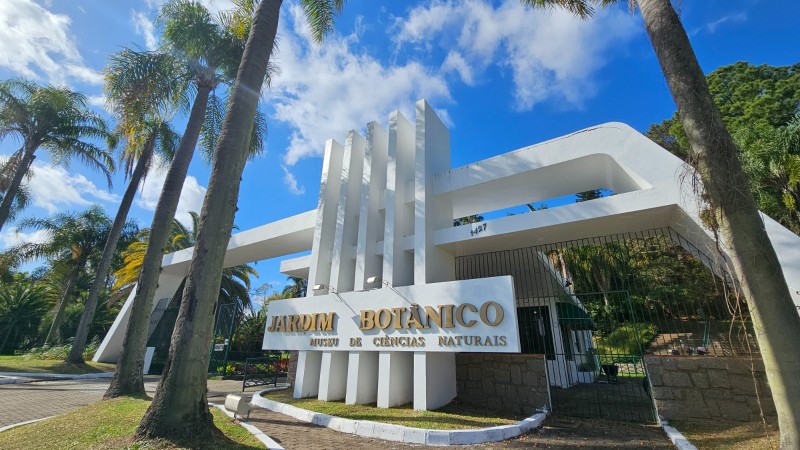 Pórtico entrada em concreto da cor branca e letras douradas com o nome jardim botânico. 