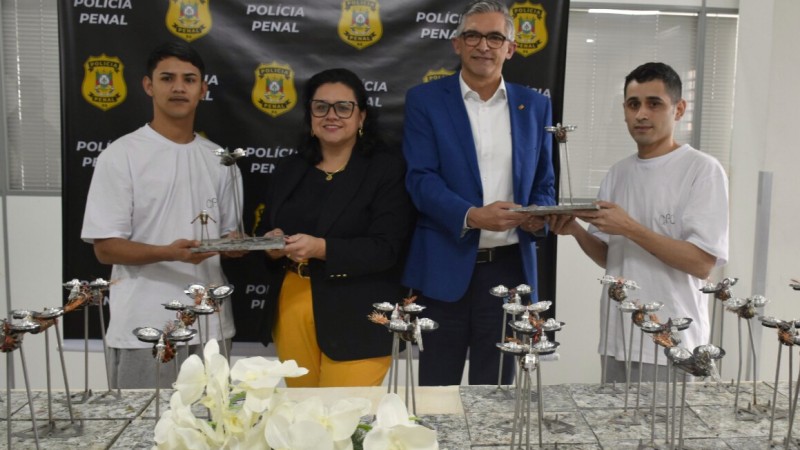 Secretários em pé recebendo dos apenados os trófeus numa entrega simbólica.