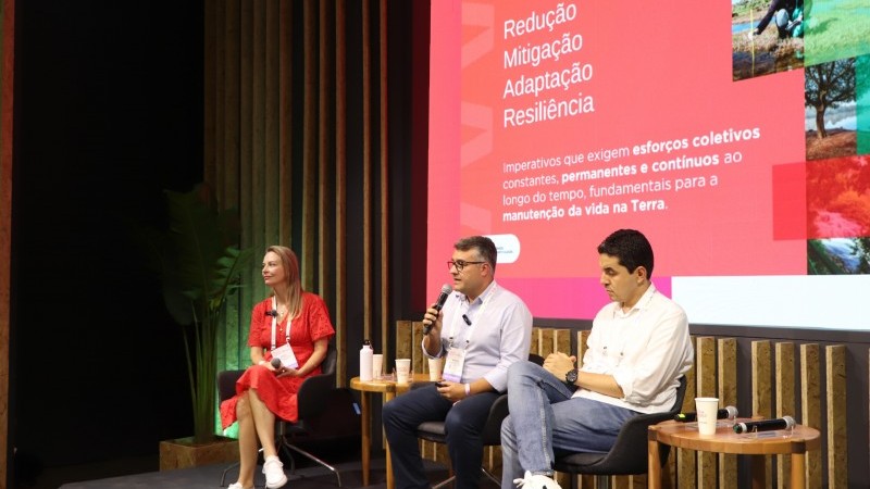 Foto dos três palestrantes sentados no palco em frente ao painel com a apresentação sobre o Roadmap Climático