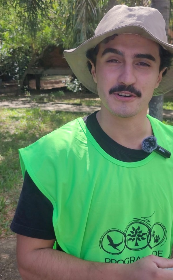 wagner, voluntário do programa, olha para câmera. ele está de chapéu caramelo, camiseta preta e colete verde do programa de voluntário. 