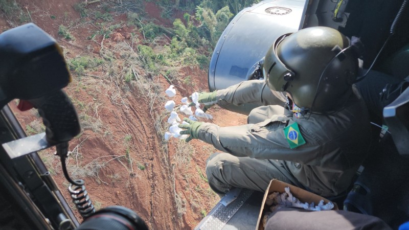 Imagem aérea de um homem do exército uniformizado e de capacete, jogando as bombas de sementes em área sem vegetação