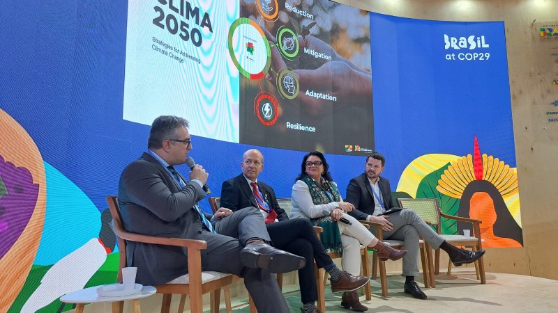 na imagem, há um painel atrás com a marca do proclima. na frente, em cima do palco, integrantes do RS olham para o moderador.