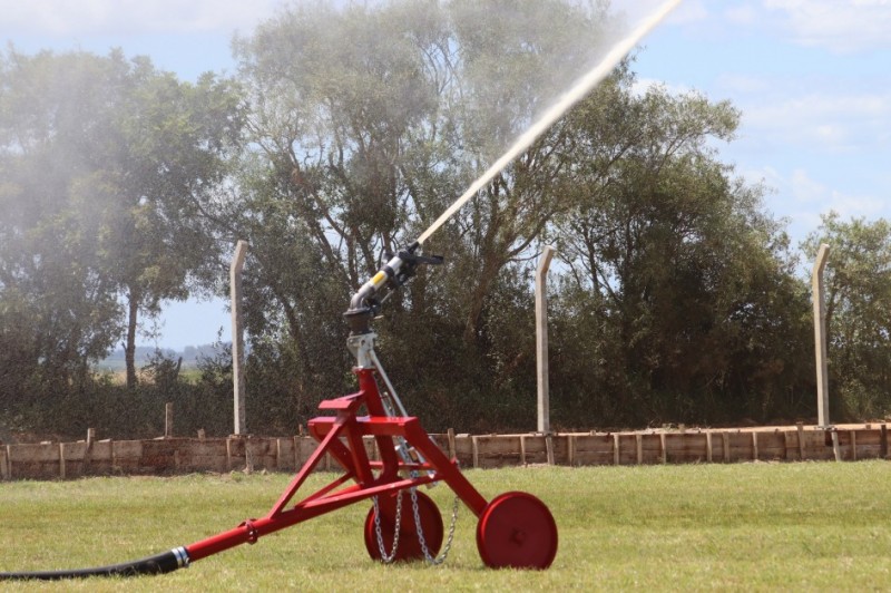 Somente um jato de irrigação, pintado de vermelho, jorra água para o alto, em um campo verde, em um dia ensolarado.