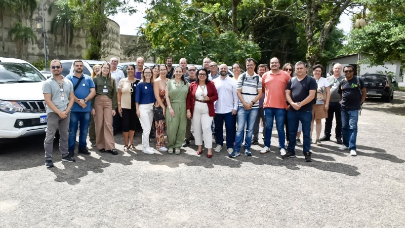 na foto o grupo de gestores, junto com a secertária marjoire, sorriem para a câmera. eles estão agrupados ao centro da imagem. ao fundo, veículos brancos, que foram entregues para as unidades de conservação.