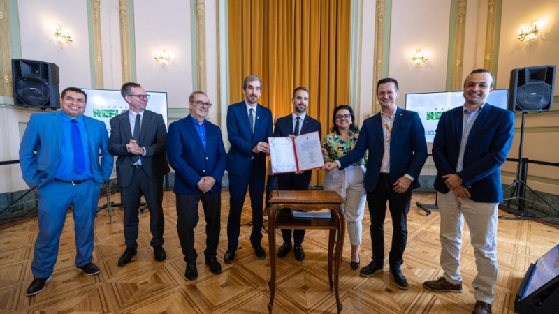 na imagem, integrantes do governo e das empresas parceiras sorriem e mostram o termo do projeto reflora que foi assinado.