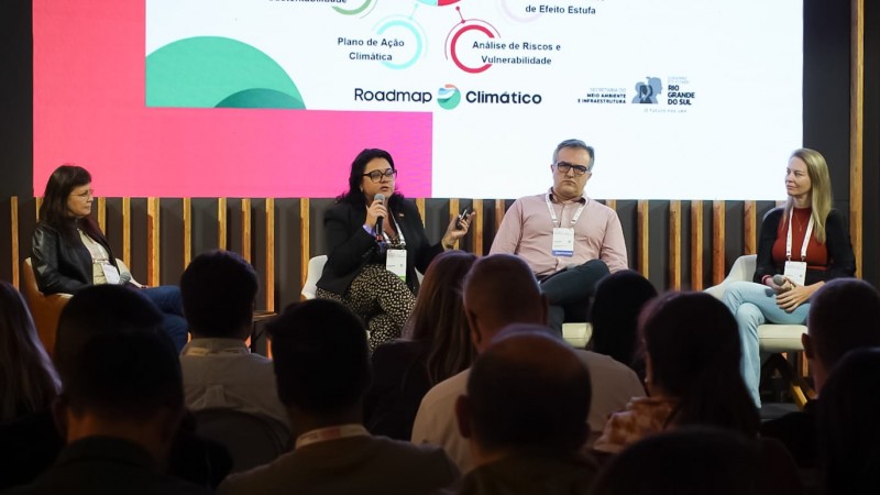 Na imagem, secretária Marjoire está com o microfone na mão palestrando para um público de pessoas. ao lado da secretária, a representante do IEDE e do Iclei. a coordenadora do clima da sema também está no palco.