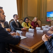 na imagem, governador aparece em primeiro plano. ao centro, uma mesa com plaquinhas brancas e, ao fundo, uma tv com o escrito: decreto estdual do bioma pampa. ao lado direito, o progurador geral alexandre saltz. do outro lado da mesa, a secretária marjorie vestida com um terno amarelo.